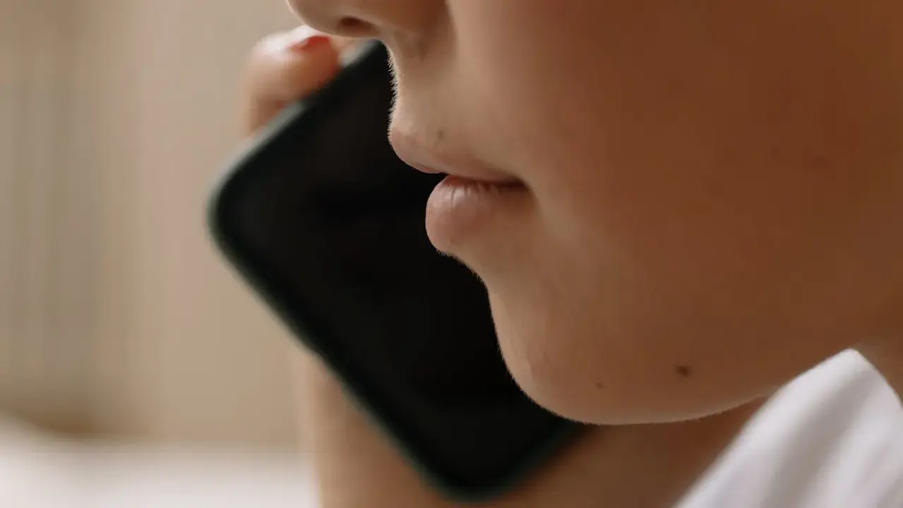 Närbild på en person som pratar i en iPhone. Kanske vill personen spela in telefonsamtal på sin iPhone för att minnas viktiga detaljer.
