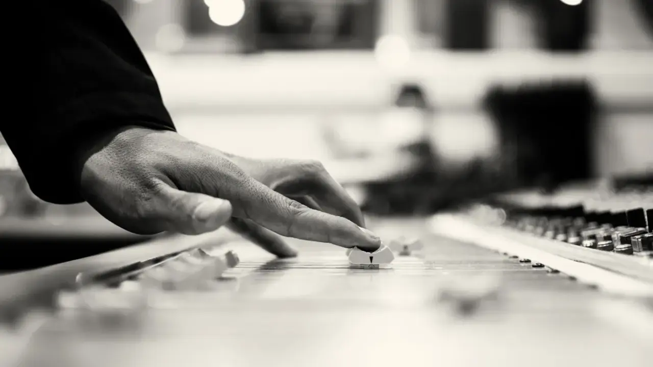Händer justerar reglage på en mixer för att kopiera musik. Ljuset skapar en drömsk atmosfär.