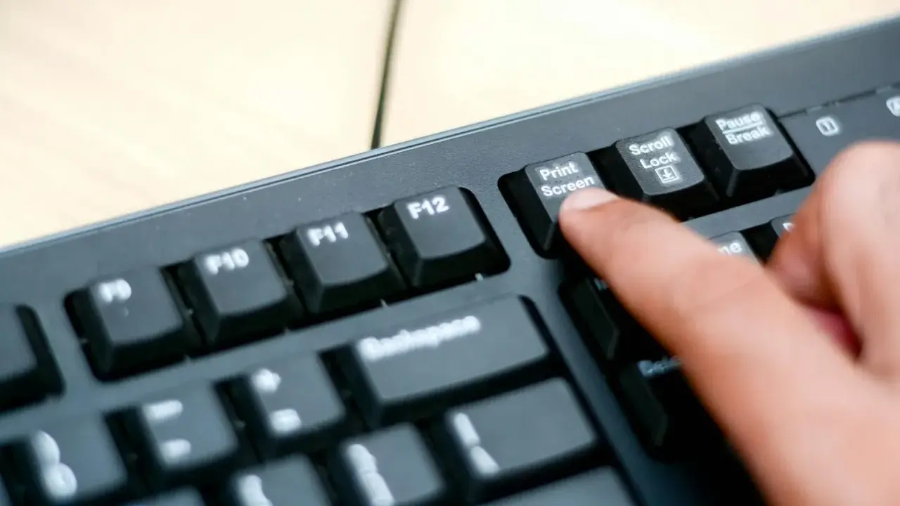 En finger trycker på "Print Screen"-knappen på ett tangentbord. Så här tar man screenshot på datorn.