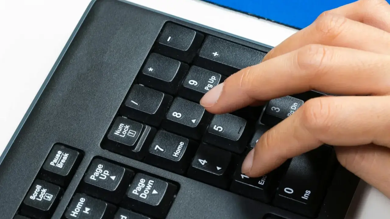 En hand trycker på siffertangenten 5 på ett numeriskt tangentbord. Kanske för att skriva in ett snabel a i ett mejl.