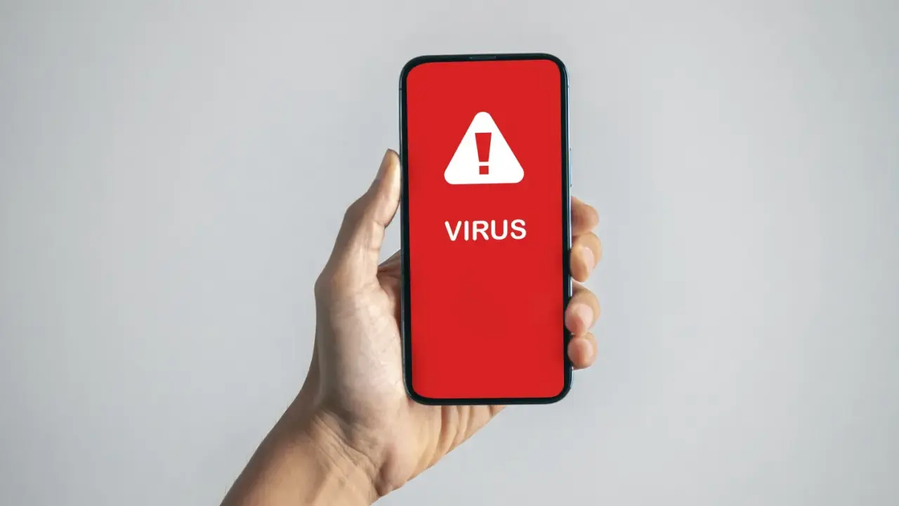 En hand håller upp en mobil med en röd skärm som varnar: "VIRUS".