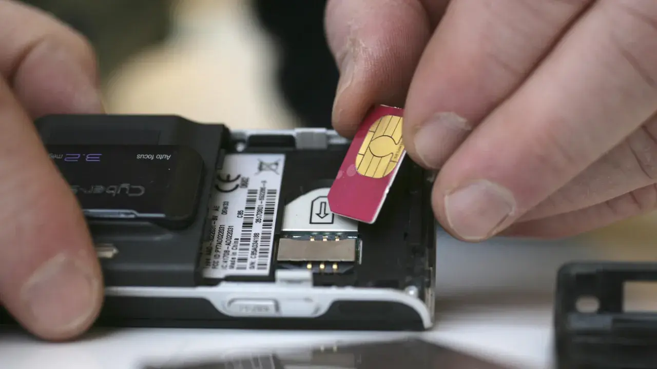 Händer sätter i ett oregistrerat kontantkort i en äldre mobiltelefon.