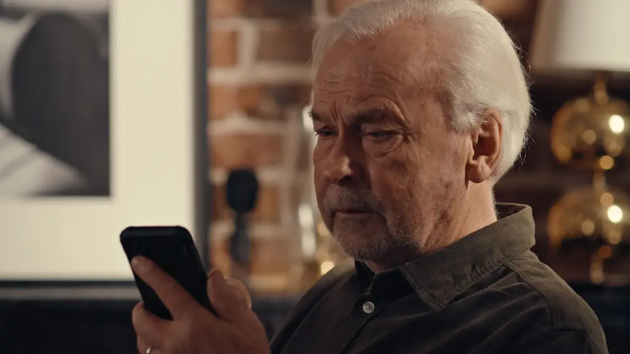 Äldre man tittar bekymrat på sin mobil, kanske efter ett tele2 bluff-sms.