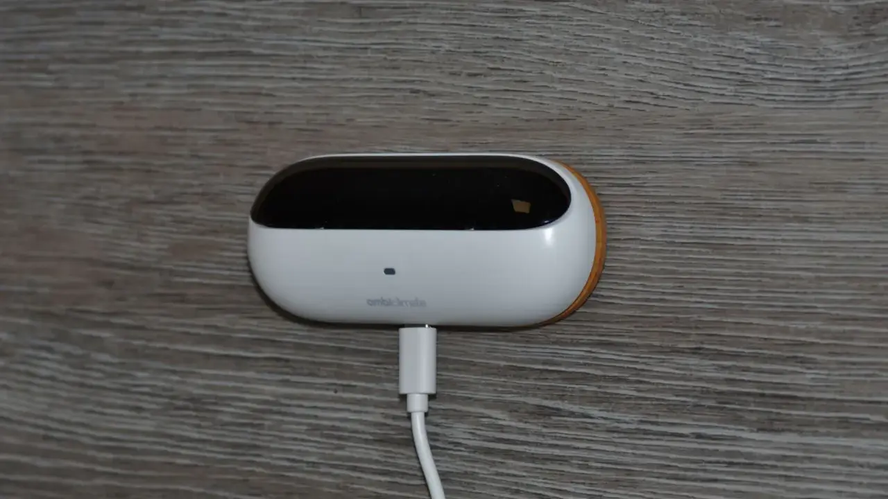 En vit, oval enhet med en svart topp, märkt "ambiclimate", är ansluten till en vit kabel. Den sitter på en träliknande yta och bidrar till ett uppkopplat hem.