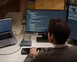En person kodar på en MacBook Air med flera skärmar.