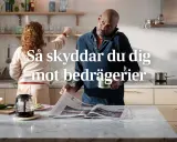 Man i köket pratar i telefon och läser tidningen, medan en kvinna plockar på hyllan. Texten "Så skyddar du dig mot bedrägerier" antyder att "vad betyder cyber" är en viktig fråga för att undvika bedrägerier.