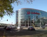 En modern glasbyggnad med stor Vodafone-logotyp, en livlig stadsgata med bilar och trafikljus. Vodafone Sverige syns tydligt.