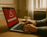 En varning om ransomware visas på en laptop. En person skriver på tangentbordet, en kaffekopp står bredvid.