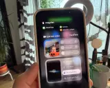 En person håller upp en iPhone som visar en skärm för gruppsamtal via FaceTime. Inställningar för ljud och video visas.