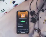 En mobil med Spotify-appen visar ljudboken "Bullerbyboken" av Astrid Lindgren, redo för insomningstimer. Hörlurar ligger bredvid.