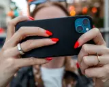 En person med röda naglar håller en iPhone. Tänk på att spionprogram iPhone kan vara ett hot mot din integritet.