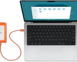 En orange extern hårddisk är ansluten till en MacBook. Perfekt för att backup mac.