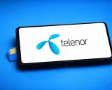En blå Telenor simkort ligger bredvid en smartphone med Telenors logotyp på skärmen.
