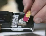 Händer sätter i ett oregistrerat kontantkort i en äldre mobiltelefon.