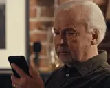 Äldre man tittar bekymrat på sin mobil, kanske efter ett tele2 bluff-sms.