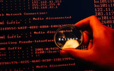 En hand håller ett förstoringsglas över en datorskärm. Förstoringsglaset visar ordet "Malware", vilket indikerar skadlig kod som döljer sig i systemets loggar.