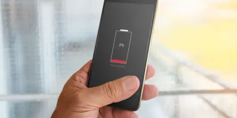 En hand håller en mobil med lågt batteri, 3%. Dags att kolla vilka appar som drar mest batteri.