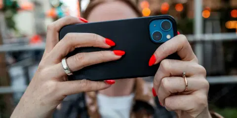 En person med röda naglar håller en iPhone. Tänk på att spionprogram iPhone kan vara ett hot mot din integritet.