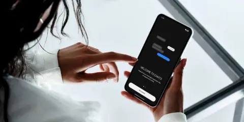 En person håller en mobiltelefon där en chattapp visas. Texten "WELCOME TO CHATS" och "Get started" syns, vilket antyder att man kan skapa grupp sms.