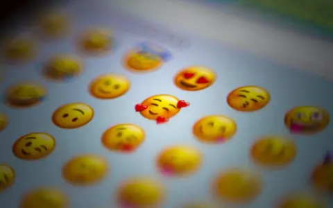 En närbild på en skärm med många gula emoji-ansikten. Ett emoji-ansikte med hjärtögon och ett annat med kyssmun syns tydligt.