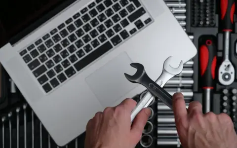 Händer håller skiftnycklar över en laptop, redo att fixa ett Windows 11-problem. Verktygslåda synlig.