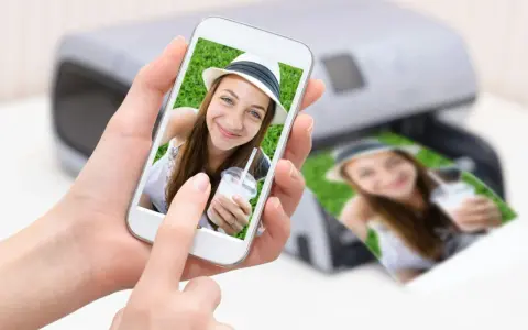 En person håller en mobil med en bild på en leende tjej med hatt. Bredvid syns en utskrift av samma bild från en skrivare. Enkelt att skriva ut från mobilen!
