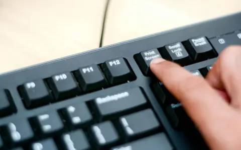 En finger trycker på "Print Screen"-knappen på ett tangentbord. Så här tar man screenshot på datorn.