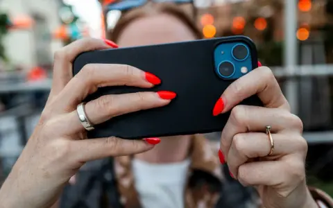 En person med röda naglar håller en iPhone. Tänk på att spionprogram iPhone kan vara ett hot mot din integritet.