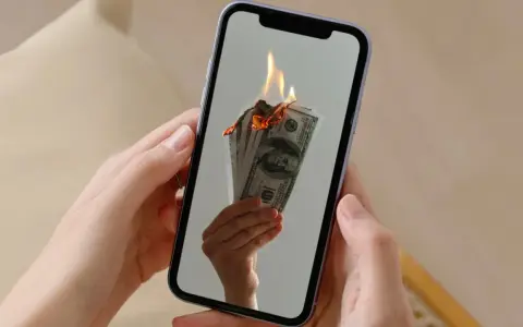 En hand håller en mobil där sedlar brinner. Kanske en bild av en misslyckad apple återbetalning.