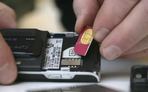 Händer sätter i ett oregistrerat kontantkort i en äldre mobiltelefon.