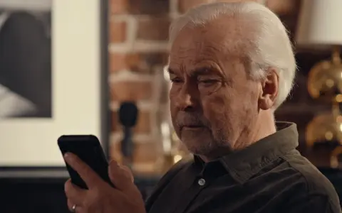 Äldre man tittar bekymrat på sin mobil, kanske efter ett tele2 bluff-sms.