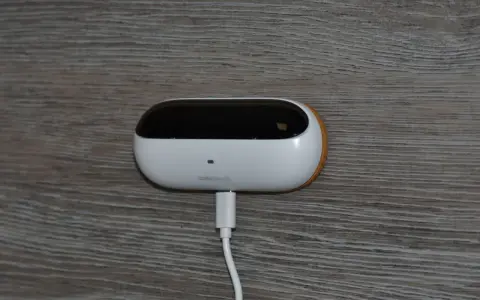 En vit, oval enhet med en svart topp, märkt "ambiclimate", är ansluten till en vit kabel. Den sitter på en träliknande yta och bidrar till ett uppkopplat hem.