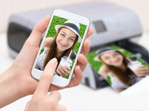 En person håller en mobil med en bild på en leende tjej med hatt. Bredvid syns en utskrift av samma bild från en skrivare. Enkelt att skriva ut från mobilen!