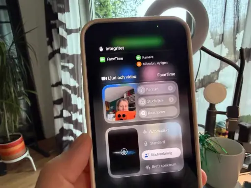En person håller upp en iPhone som visar en skärm för gruppsamtal via FaceTime. Inställningar för ljud och video visas.