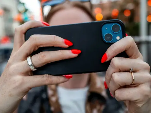 En person med röda naglar håller en iPhone. Tänk på att spionprogram iPhone kan vara ett hot mot din integritet.
