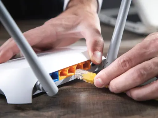 Händer kopplar in en gul nätverkskabel i en vit router, redo att byta router för bättre uppkoppling.