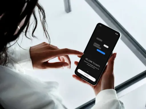 En person håller en mobiltelefon där en chattapp visas. Texten "WELCOME TO CHATS" och "Get started" syns, vilket antyder att man kan skapa grupp sms.