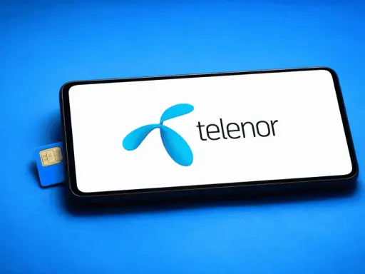 En blå Telenor simkort ligger bredvid en smartphone med Telenors logotyp på skärmen.