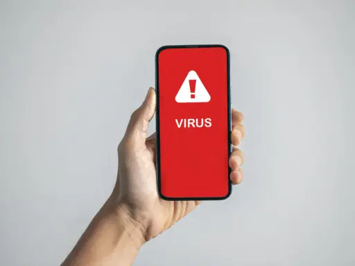 En hand håller upp en mobil med en röd skärm som varnar: "VIRUS".