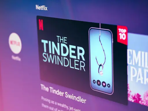 Netflix-skärmen visar "The Tinder Swindler", en dokumentär om tinder bilder på bedragare. En fiskekrok med en diamantring hänger i en mobil.