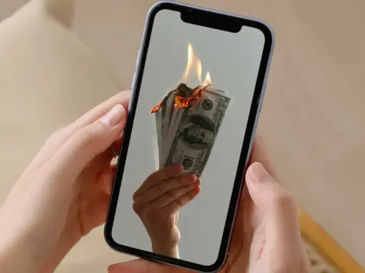 En hand håller en mobil där sedlar brinner. Kanske en bild av en misslyckad apple återbetalning.