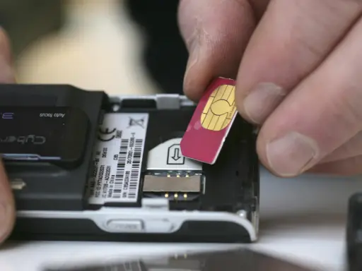 Händer sätter i ett oregistrerat kontantkort i en äldre mobiltelefon.
