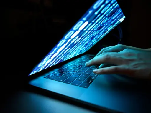Händer på ett tangentbord, skärmen visar binär kod som flödar, en visuell representation av ett cyberattack idag.