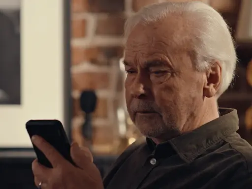 Äldre man tittar bekymrat på sin mobil, kanske efter ett tele2 bluff-sms.