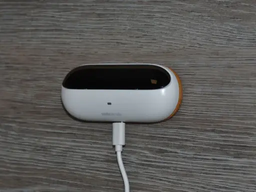 En vit, oval enhet med en svart topp, märkt "ambiclimate", är ansluten till en vit kabel. Den sitter på en träliknande yta och bidrar till ett uppkopplat hem.