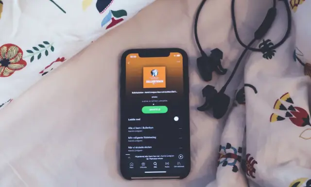 En mobil med Spotify-appen visar ljudboken "Bullerbyboken" av Astrid Lindgren, redo för insomningstimer. Hörlurar ligger bredvid.