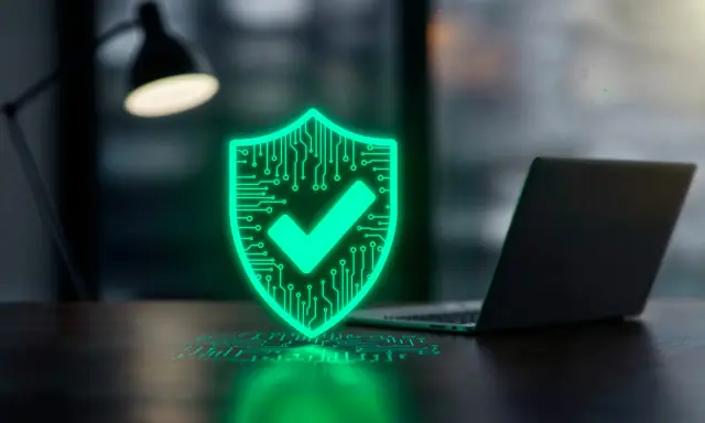 En lysande grön sköld med ett kryss symboliserar ett bra virusprogram. Bredvid står en laptop, redo att skyddas.