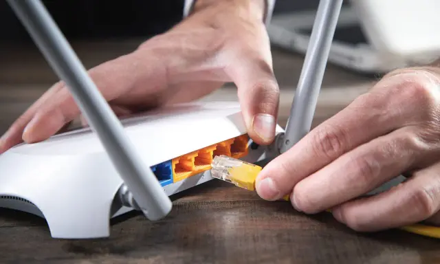 Händer kopplar in en gul nätverkskabel i en vit router, redo att byta router för bättre uppkoppling.