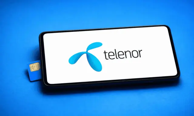 En blå Telenor simkort ligger bredvid en smartphone med Telenors logotyp på skärmen.