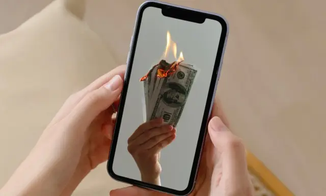 En hand håller en mobil där sedlar brinner. Kanske en bild av en misslyckad apple återbetalning.